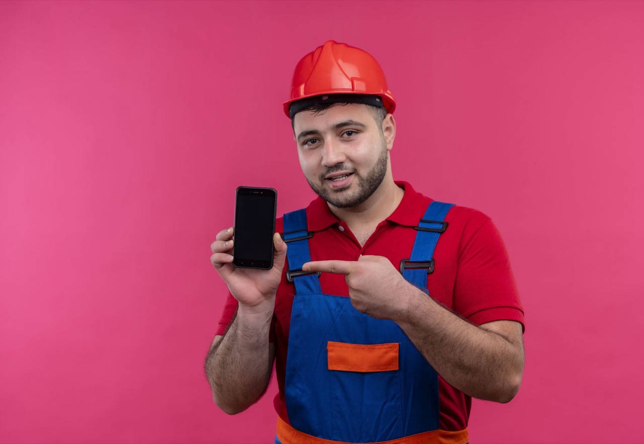 Tradesman in a red safety helmet and hi-vis holding and pointing at a smartphone